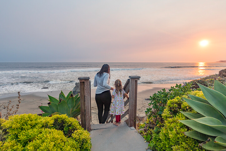 A mother and daughter enjoy the breathtaking sunset from the beach access point at Cayucos Beach Inn, creating a memorable family moment.