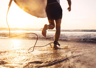 A man runs into the ocean waves with his surfboard during a vibrant sunset, capturing the essence of adventure at Cayucos Beach.