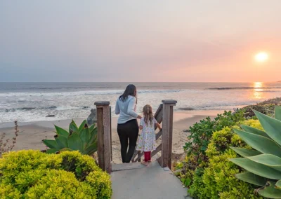 A mother and daughter enjoy the breathtaking sunset from the beach access point at Cayucos Beach Inn, creating a memorable family moment.